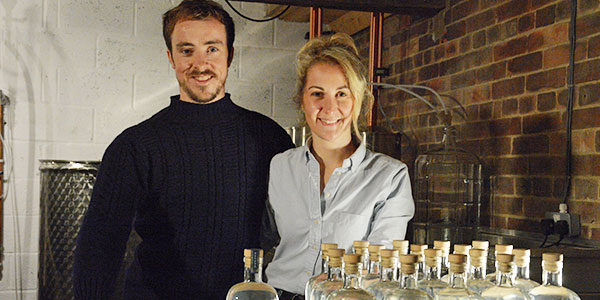 Picture of Jess Slater (a woman) and Luke Pentith (a man) at Whitby Distillery, with a number of Whitby Gin bottles in front of them.