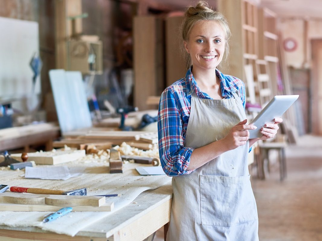 A woman in an apron looking at the camera, she is in a woodwork studio.